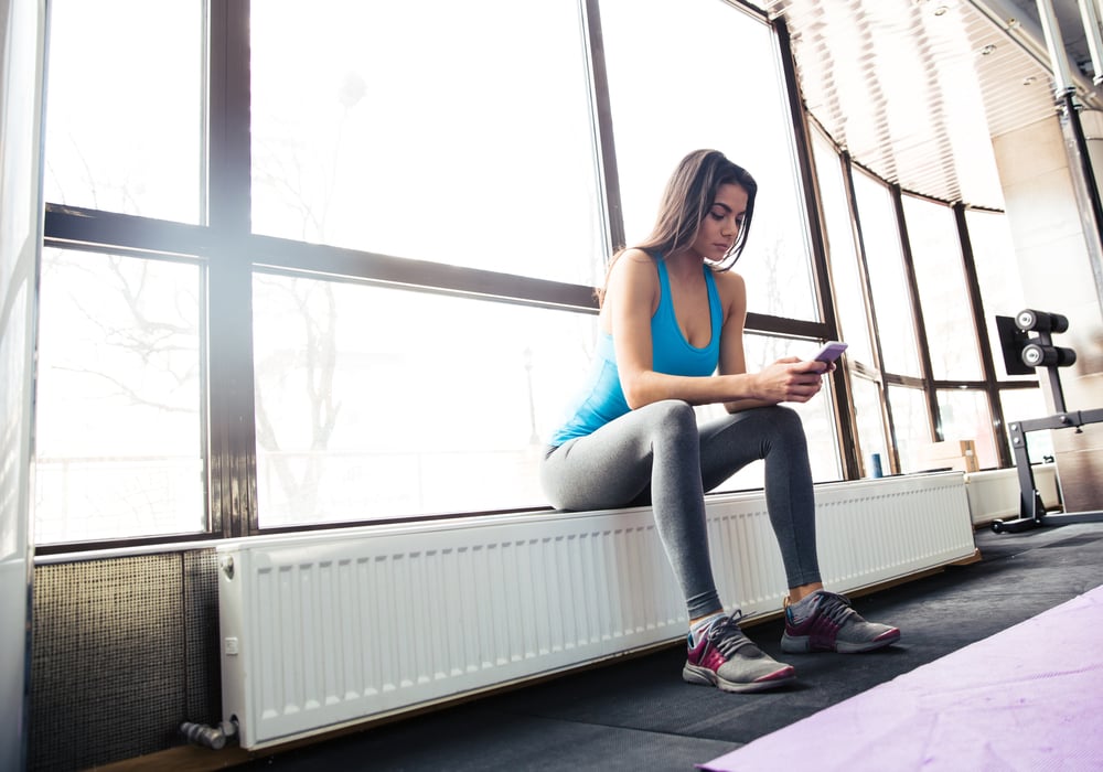 Young fit woman using smartphone at gym